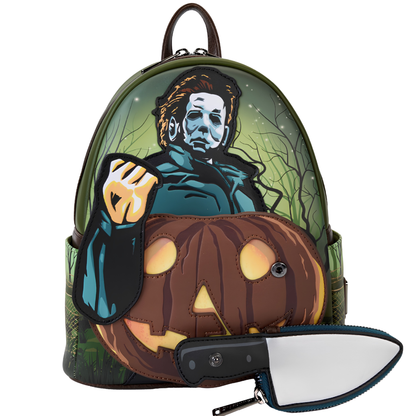 A Halloween-themed backpack featuring a graphic of Michael Myers behind a large jack-o'-lantern, with a matching knife-shaped pouch and small knife placed in front on a plain white background.